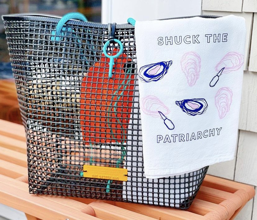 A white tea towel that reads "Shuck the Patriarchy" hangs on an oyster bag