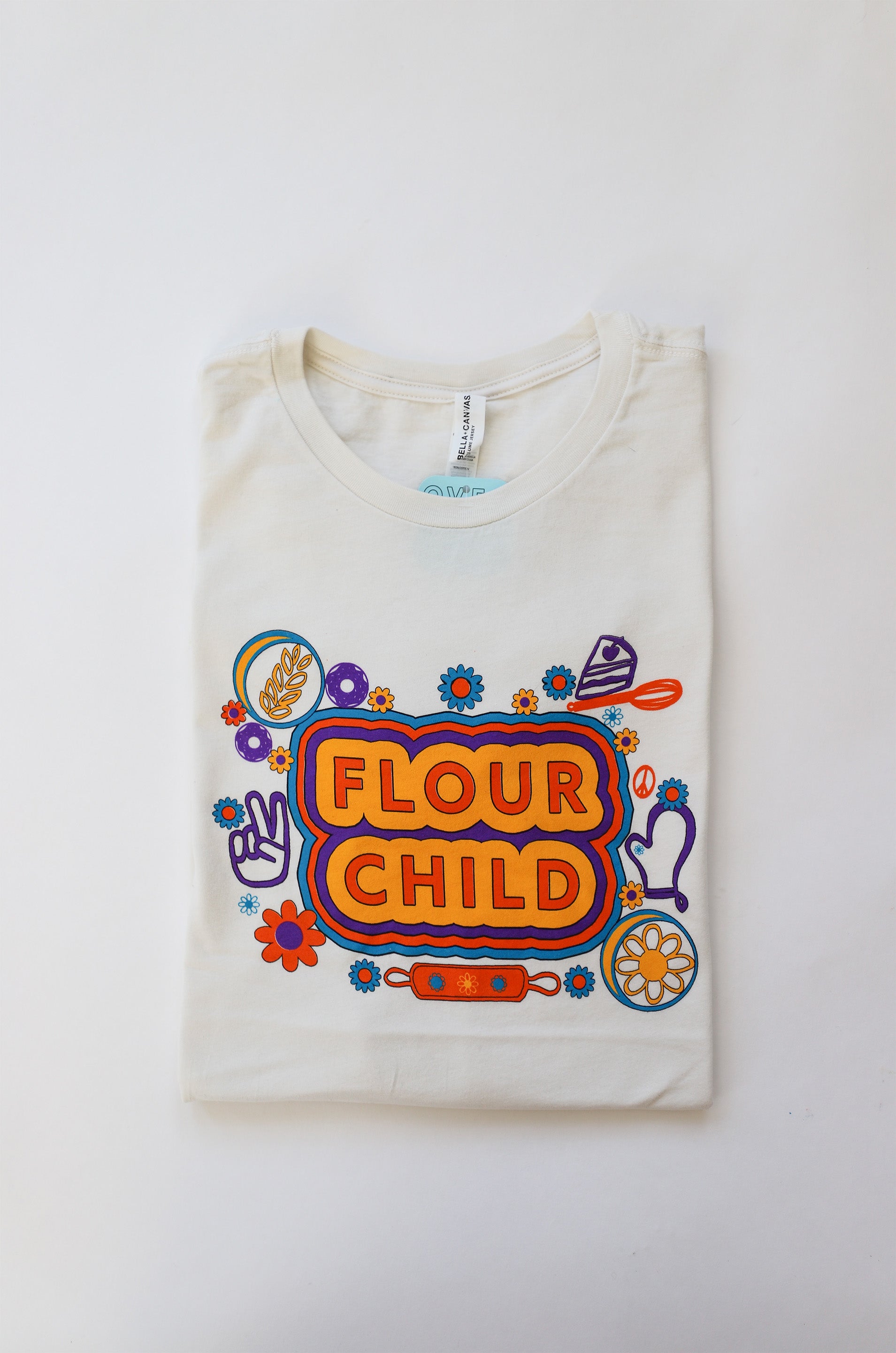 A folded white tee with the words Flour Child and yellow, orange, blue and purple illustrations