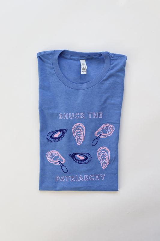A folded bright blue t-shirt that reads "Shuck the Patriarchy" with oyster illustrations 