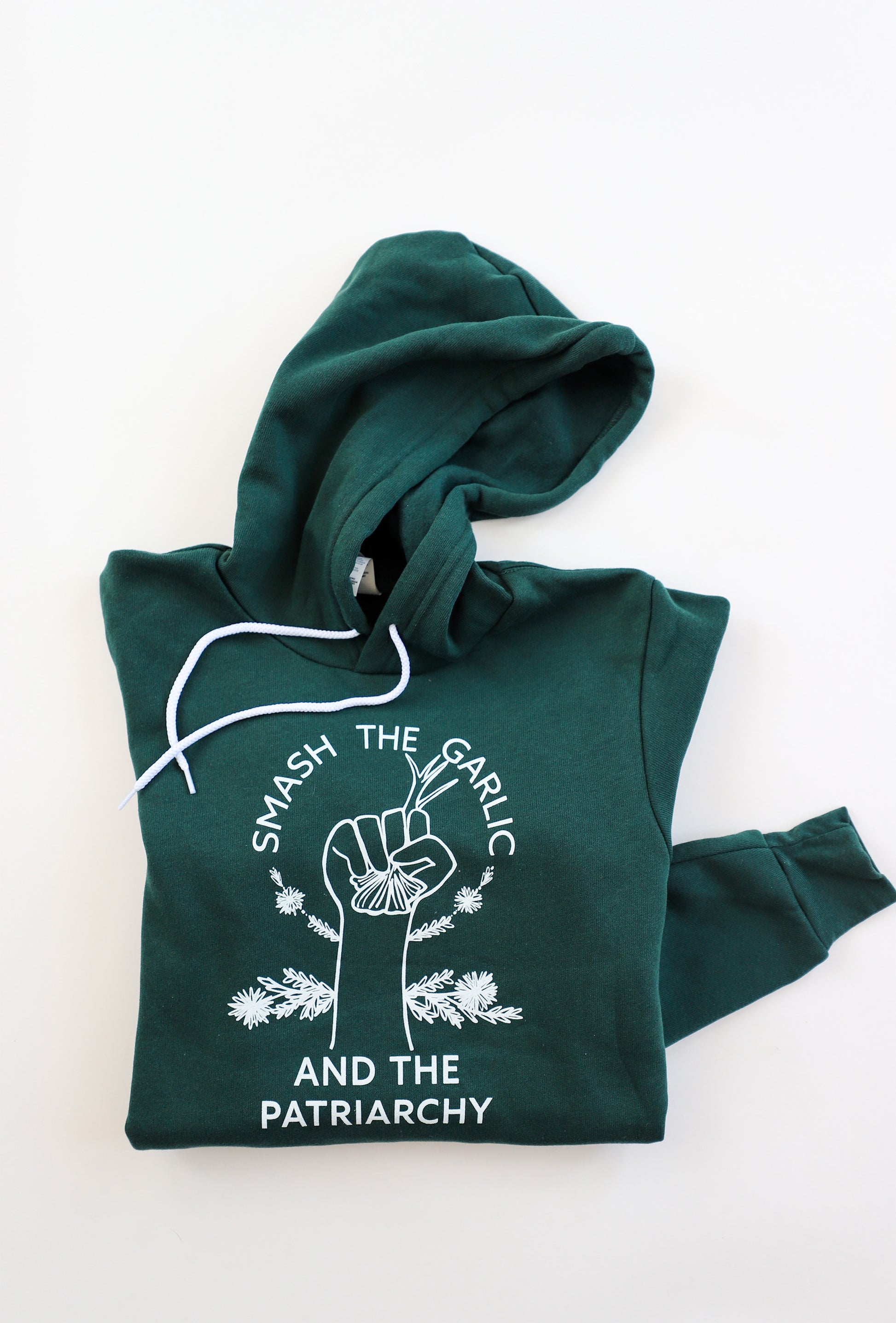 A folded forest green hoodie with the words "Smash the Garlic and the Patriarchy" with an illustration of a hand holding garlic