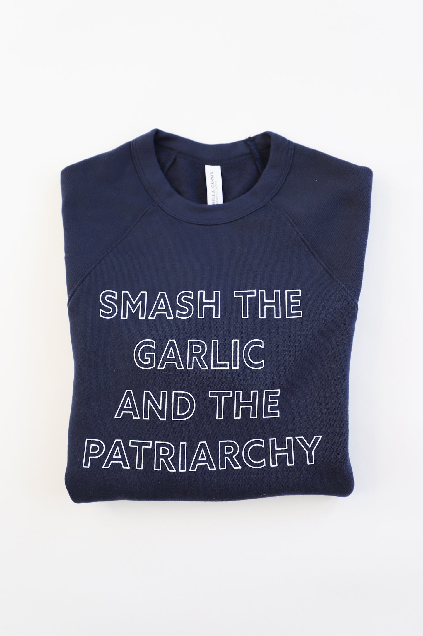 A folded navy blue crewneck reads "Smash the Garlic and the Patriarchy" in white block letters