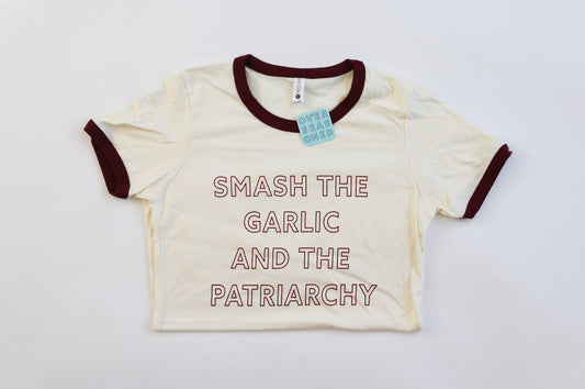 An off-white ringer t-shirt with the words "Smash the Garlic and the Patriarchy" in maroon block letters
