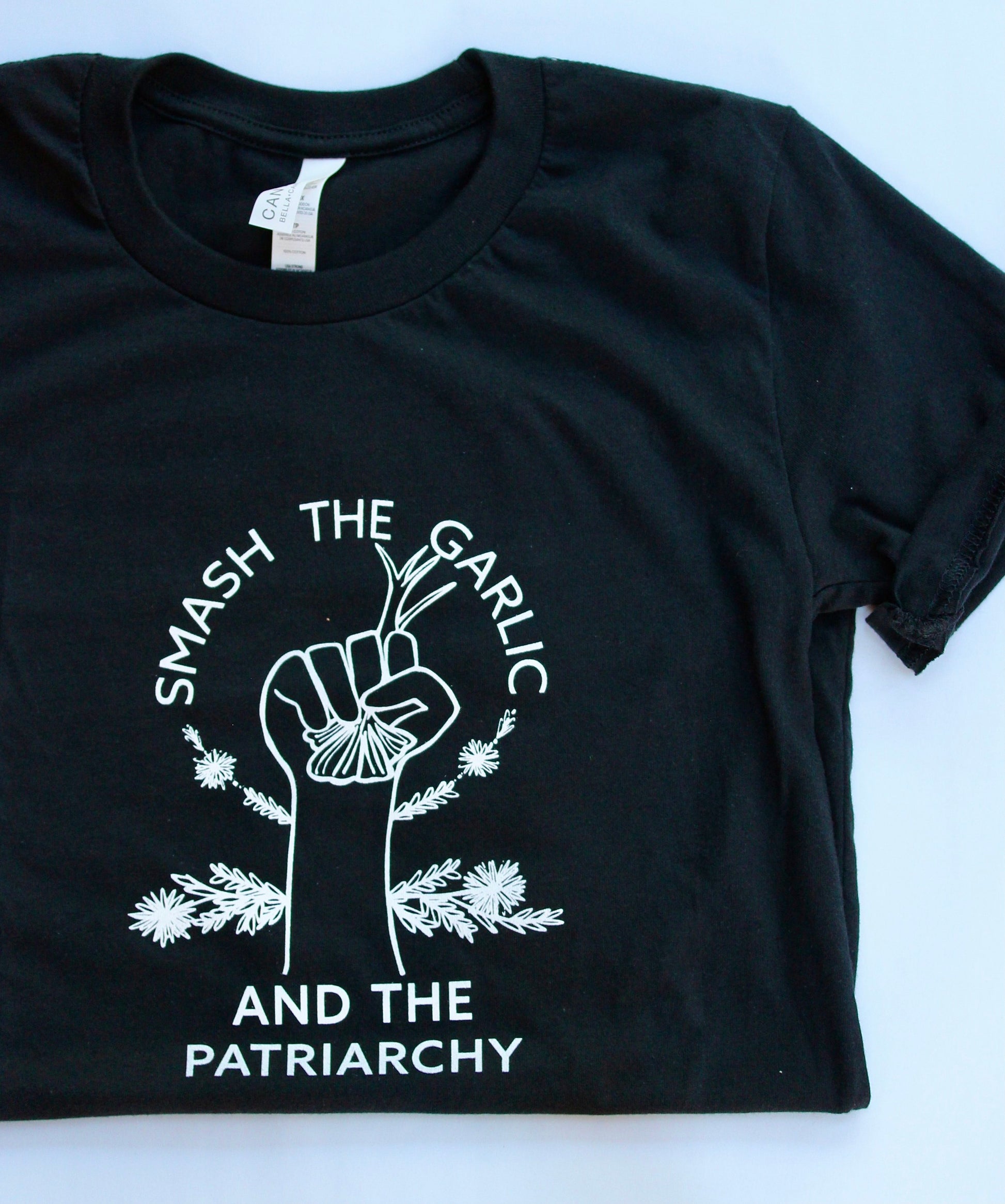 A black t-shirt reads "Smash the Garlic and the Patriarchy" with an illustration of a hand holding garlic in white