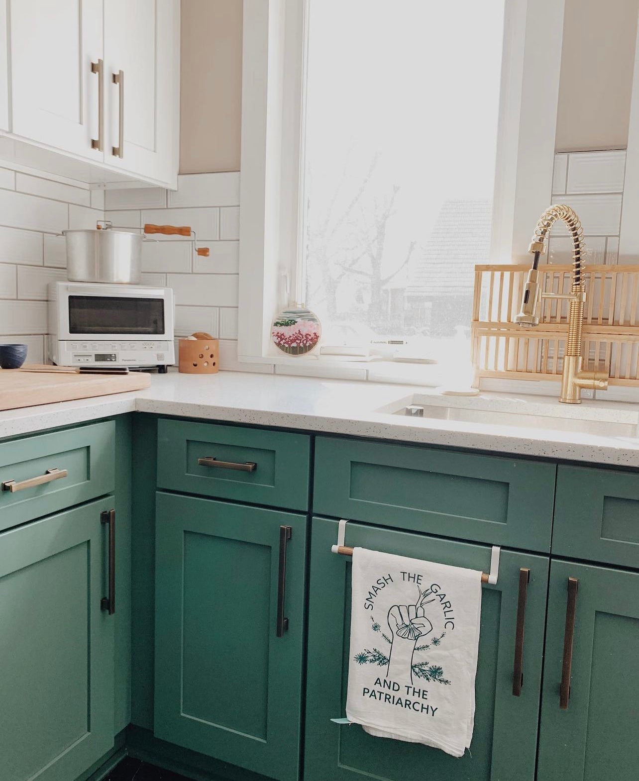 A "Smash the Garlic and the Patriarchy" tea towel hangs in a kitchen with green cabinets