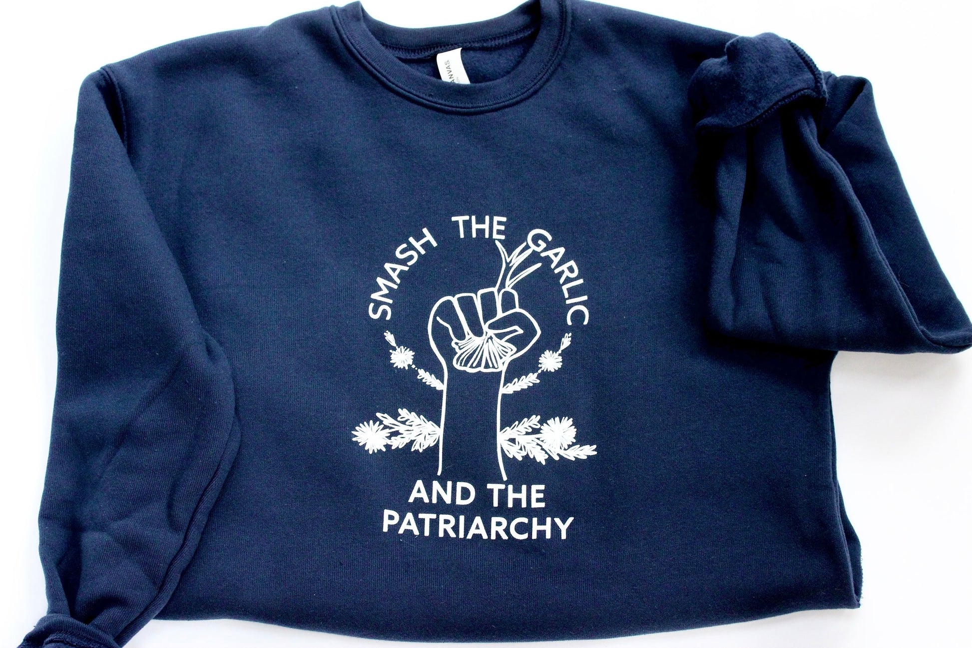 A navy blue crewneck with the words "Smash the Garlic and the Patriarchy" and an illustration of a hand holding garlic