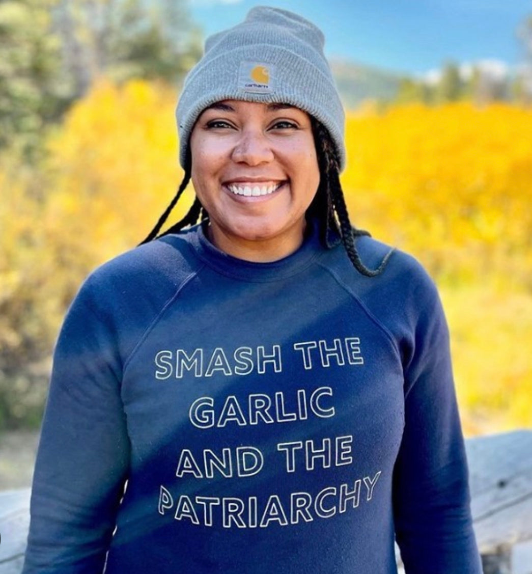 A woman wears a navy blue "Smash the Garlic and the Patriarchy" sweatshirt with a gray beanie
