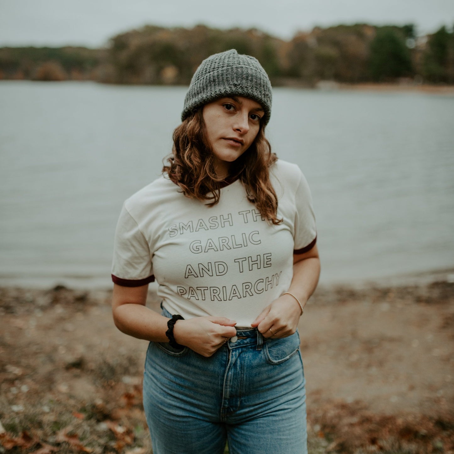 A woman wears a "Smash the Garlic and the Patriarchy" ringer tee with jeans and a gray beanie