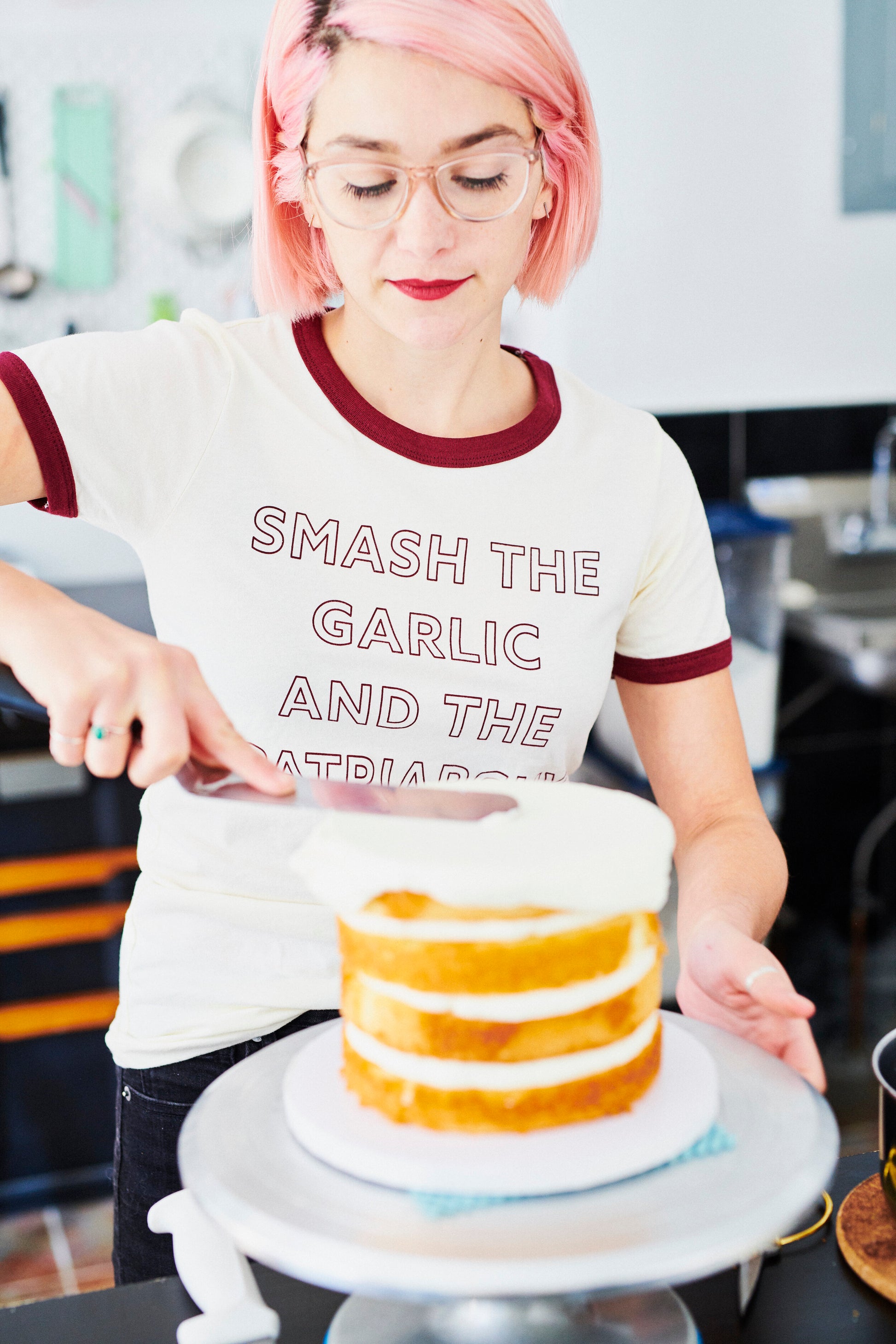 A woman wearing a "Smash the Garlic and the Patriarchy" ringer tee frosts a cake