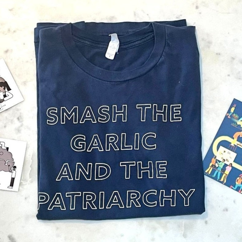 A folded navy blue t-shirt reads "Smash the Garlic and the Patriarchy" in white block letters